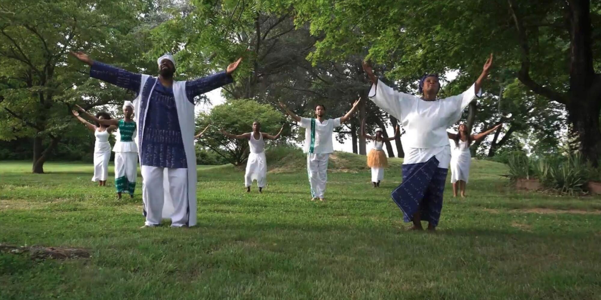 Dr. Nance with his mentor Dr. Kariamu Welsh and others dancing in a grassy meadow