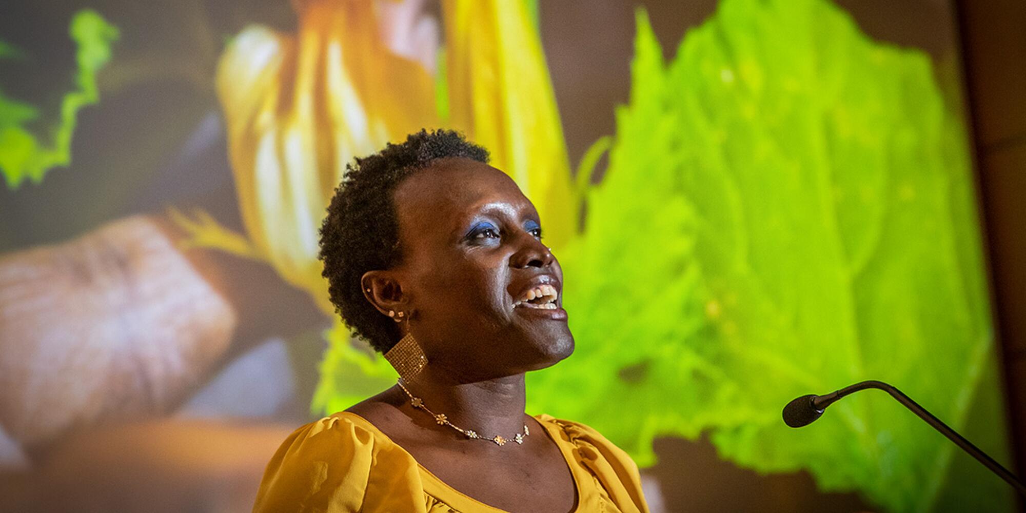 Dr Ngumbi speaking in a yellow shirt with plant presentation behind her