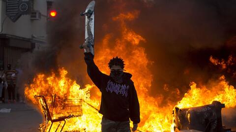 protester holding up skateboard in front of fires from the protests