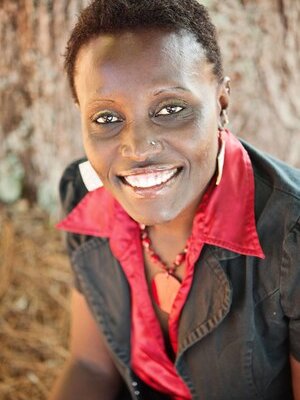 Dr. Ngumbi smiling in a red button up shirt with a black blazer jacket over it.